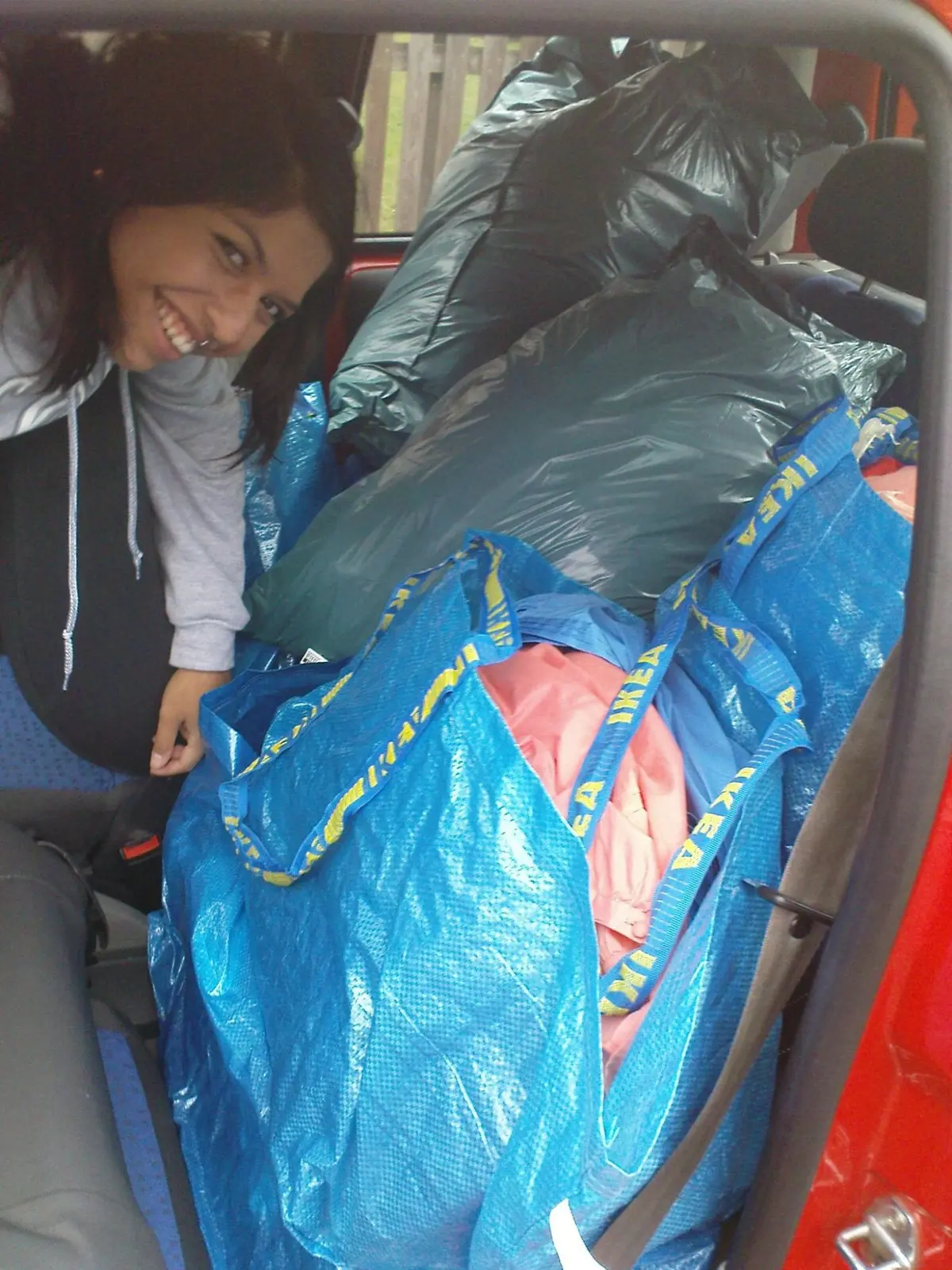 Heidi lacht neben einem Auto voller blauer Ikea-Taschen und Säcke mit Klamotten