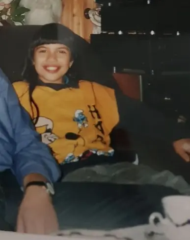 Heidi als Kind im gelben Schlümpfe-Pullover, lachend auf dem Sofa